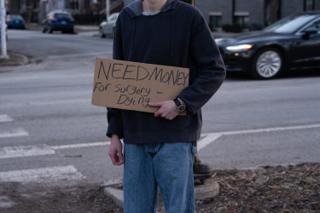 Close on the hand-lettered cardboard sign carried through the scene
