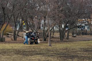 Two crew wheeling the equipment cart across the park, bare trees and fallen logs beyond