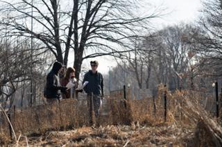 Three of the company walking the fence line with pages in hand, dry grass and bare trees around them
