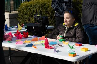 Paper cranes, folded flowers and boxes spread across the prop table, a crew member sitting with them in the sun