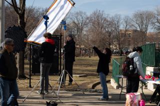 A white bounce board raised on stands and angled into the low sun, crew steadying it from either side