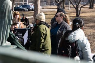 The company crowded around the camera and its monitor at the base of the park statue