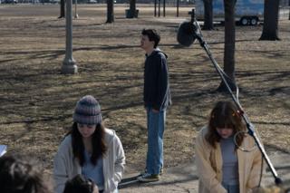 The young actor alone on the grass mid-take, the boom swung in overhead and two of the cast in the foreground