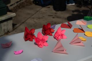 Origami flowers, cranes and folded paper boats laid out in rows on the white prop table