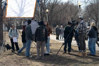 The unit clustered around a large diffusion frame and round reflector, camera up on sticks beside the park path