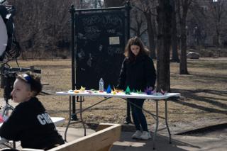 A crew member setting out the folded cranes along the prop table in front of the chalkboard