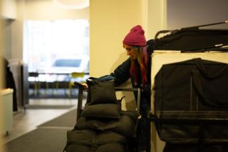 Crew member in a knit beanie loading sandbags and equipment cases onto a cart