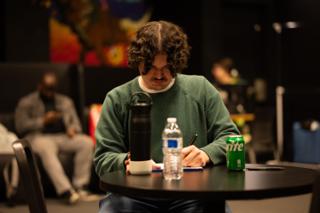 Actor making notes at a table between setups while the room rests behind him