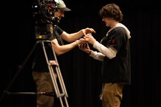 Camera operator handing a prop across to an actor beside the tripod-mounted camera