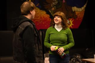 Two performers laughing together between takes in front of the painted mural