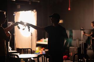 Silhouetted crew handing off gear in front of a backlit diffusion frame