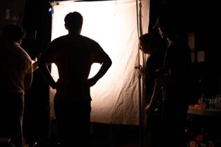 Crew member standing in silhouette against the glowing diffusion frame as the set is lit