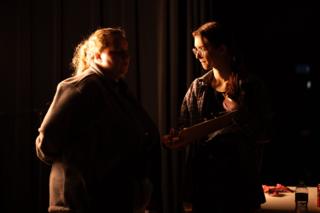 Two crew members conferring over a script under warm light on the darkened set