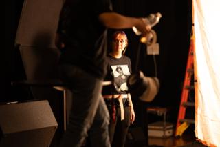 Grip carrying a lighting fixture past a performer standing beside a large diffusion frame