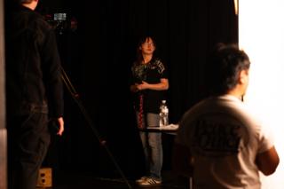 Performer waiting in a pool of light on set as the camera team look on from the shadows