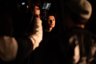 Camera operator framing a close-up of an actor lit warmly against the dark