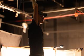 Grip reaching overhead to adjust rigging on the lighting grid above the set