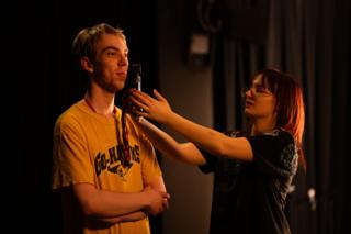 Makeup artist checking an actor's face by phone light before a take