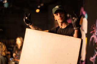 Grip holding a large white bounce card up beside the set, gloved hands on the frame