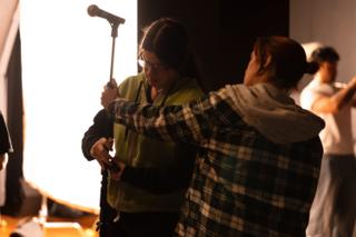 Crew adjusting a microphone stand in front of a glowing diffusion frame