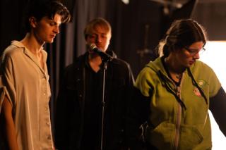 Actor at the microphone with the director and a crew member close by between setups