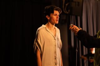 Lead actor performing at the microphone as a crew member holds a meter into frame