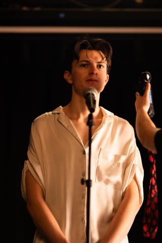 Lead actor at the microphone while a light meter is held up beside him
