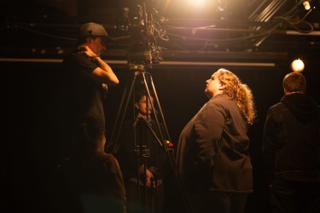 Crew gathered around the camera on its tripod, one looking up into the overhead light