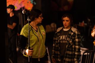 Two people in conversation on set, one holding a microphone stand, in front of a painted backdrop