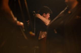 Actor glimpsed between crew shoulders as she leans in at the microphone
