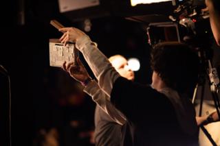 Second AC holding the clapperboard up into frame in front of the camera
