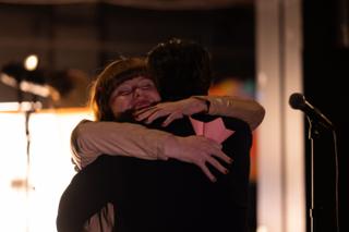 Two of the team embracing on set, one holding a folded paper star