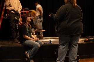 Crew member sitting on the edge of the stage during a reset, dolly track laid across the boards