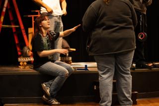Crew member on the stage edge talking a colleague through the next setup, dolly track laid behind them