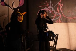 Sound recordist adjusting her headphones beside her rig in front of the neon mural