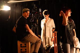 Camera operator seated at the rig between takes, an actor and crew member waiting alongside