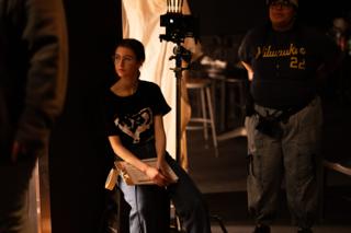 Script supervisor waiting with her notes beside the camera on the lit set