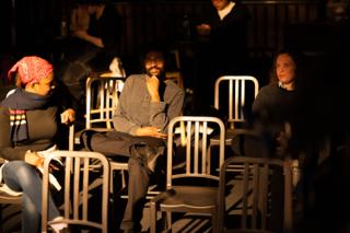 Cast and crew sitting among the stacked cafe chairs between setups