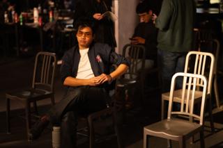 Actor waiting in a chair among the empty cafe furniture as the crew move behind him