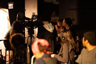 Camera and sound crew crowded around the rig while the room watches from the chairs