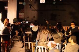 Boom operator holding the pole overhead as the crew shoot the cafe scene