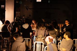 Wide of the cafe set mid-take, boom overhead and the crew ranged behind the camera