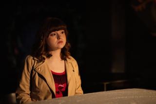 Actor in a tan jacket waiting on her mark in a pool of light