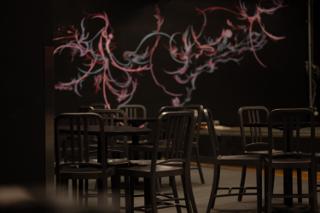 Empty cafe tables and stacked chairs on the darkened set, a pink and blue mural glowing on the wall behind