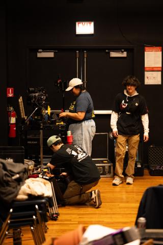 Camera team building a rig beside the equipment cart, one kneeling over a case while another checks the monitor