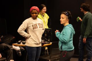 Two performers talking in the wings, gear cases and a work table behind them