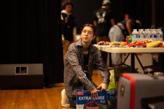 Crew member kneeling beside the craft services table setting out supplies while others pass behind