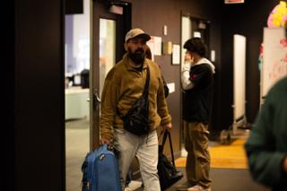 Crew member arriving through the stage doors carrying bags and a rolling case