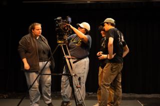 Four crew members gathered around the camera on its tripod, one reaching up to the monitor