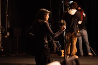 Boom operator working mid-take, the camera crew silhouetted deeper in the frame